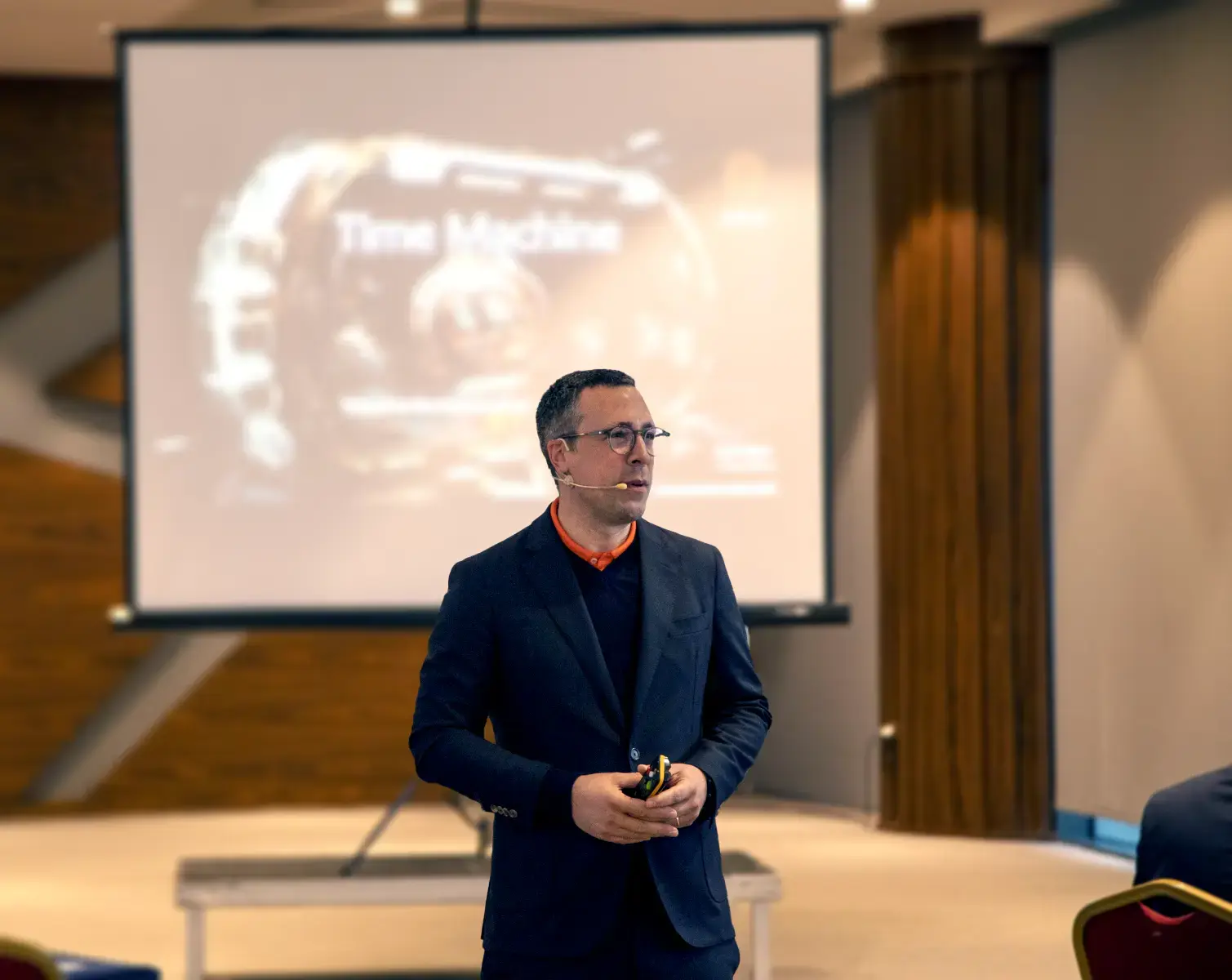 Image of Lutz Kögler talking in front of a large screen, wearing a microphone.